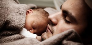 Un padre e un neonato dormono serenamente, avvolti in una coperta morbida, simbolo di cura e protezione familiare