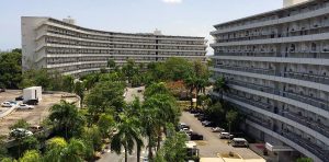 Vista aerea di due grandi condomini bianchi con balconi, circondati da palme e vegetazione  con parcheggi
