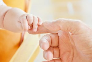 La piccola mano di un bambino afferra il dito di un adulto, simboleggiando la tutela e il mantenimento dei figli