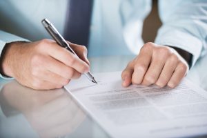 Mani di un professionista che firma un documento legale, probabilmente un testamento biologico, evidenziando la consulenza