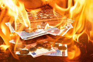 Una cassetta di legno aperta con banconote e monete in euro avvolte dalle fiamme, simboleggiando i rischi dell'usura