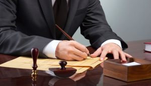 Un professionista  firma un documento legale con una penna d'oca, simbolo di lasciti testamentari e consulenza