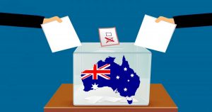 Due mani inseriscono schede elettorali in un'urna trasparente con la mappa dell'Australia e la sua bandiera, simbolo delle elezioni federali