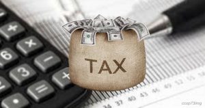 Un sacco  con la scritta TAX pieno di banconote da 100 dollari, su una calcolatrice e documenti, simboleggia la gestione dei debiti fiscali