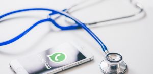 Uno smartphone con l'app WhatsApp e uno stetoscopio blu su sfondo bianco, simboleggiando la complessità legale per i medici