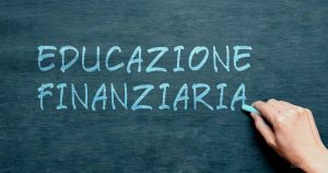 Mano che scrive EDUCAZIONE FINANZIARIA con il gesso su una lavagna, riflettendo l'importanza della consulenza legale e finanziaria